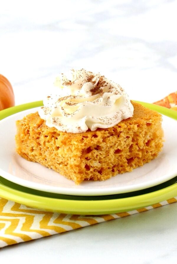 Pumpkin Angel Food Cake on plate with whip cream on top, and pumpkin in background.
