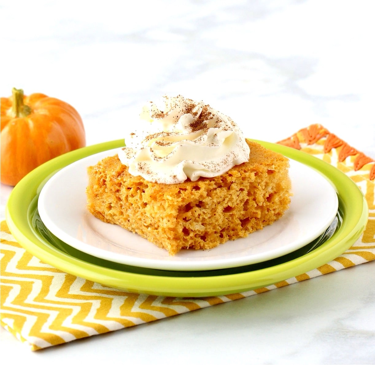 Pumpkin Angel Food Cake on plate with whip cream on top, and pumpkin in background.