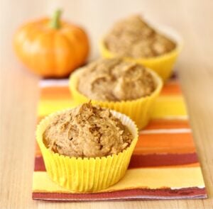 Three cake mix pumpkin muffins on a napkin, with small pumpkin in background.