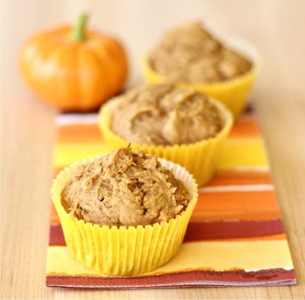 Three cake mix pumpkin muffins on a napkin, with small pumpkin in background.