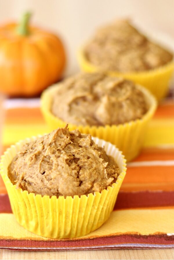 Three cake mix pumpkin muffins on a napkin, with small pumpkin in background.