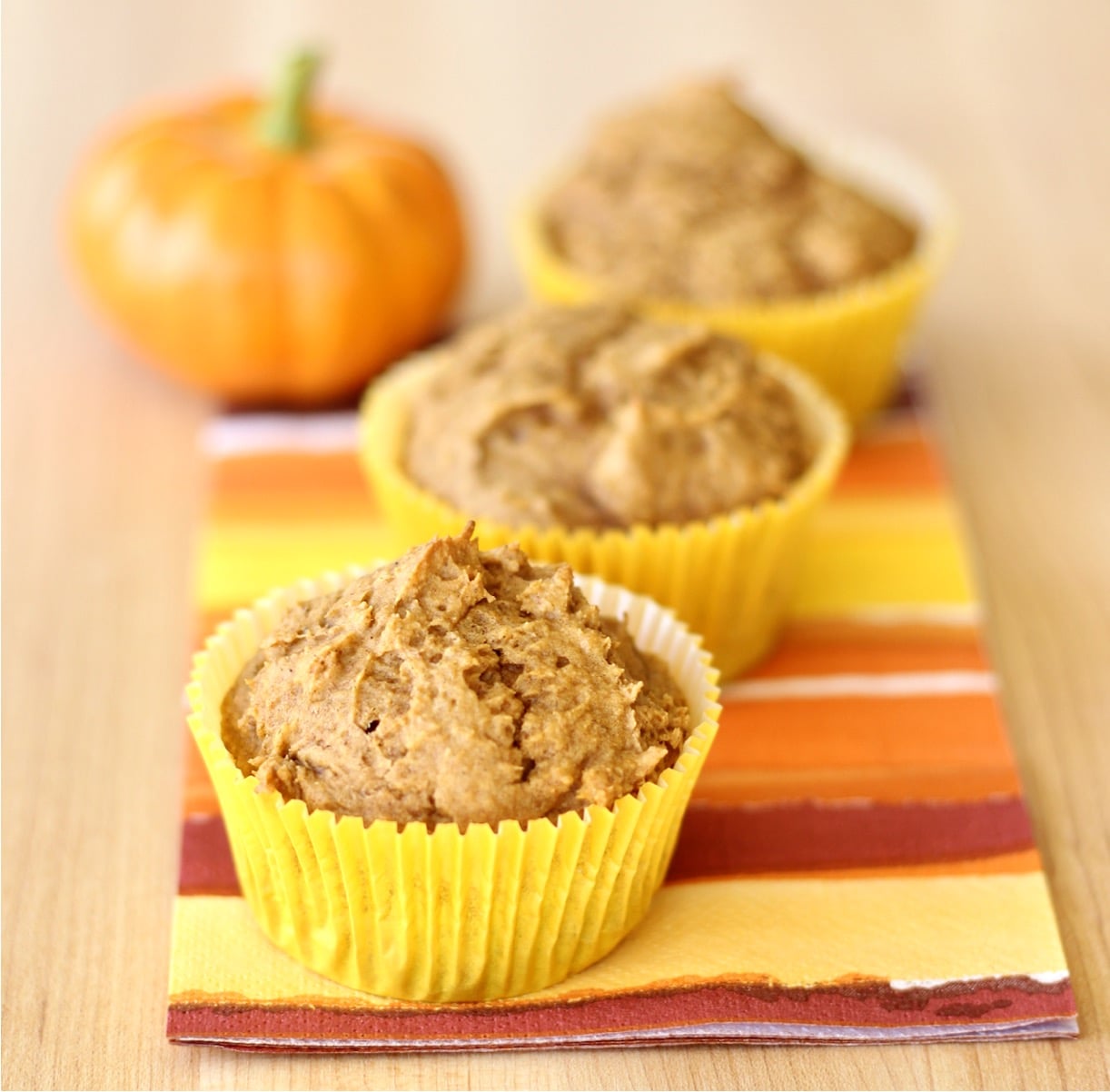 Three cake mix pumpkin muffins on a napkin, with small pumpkin in background.