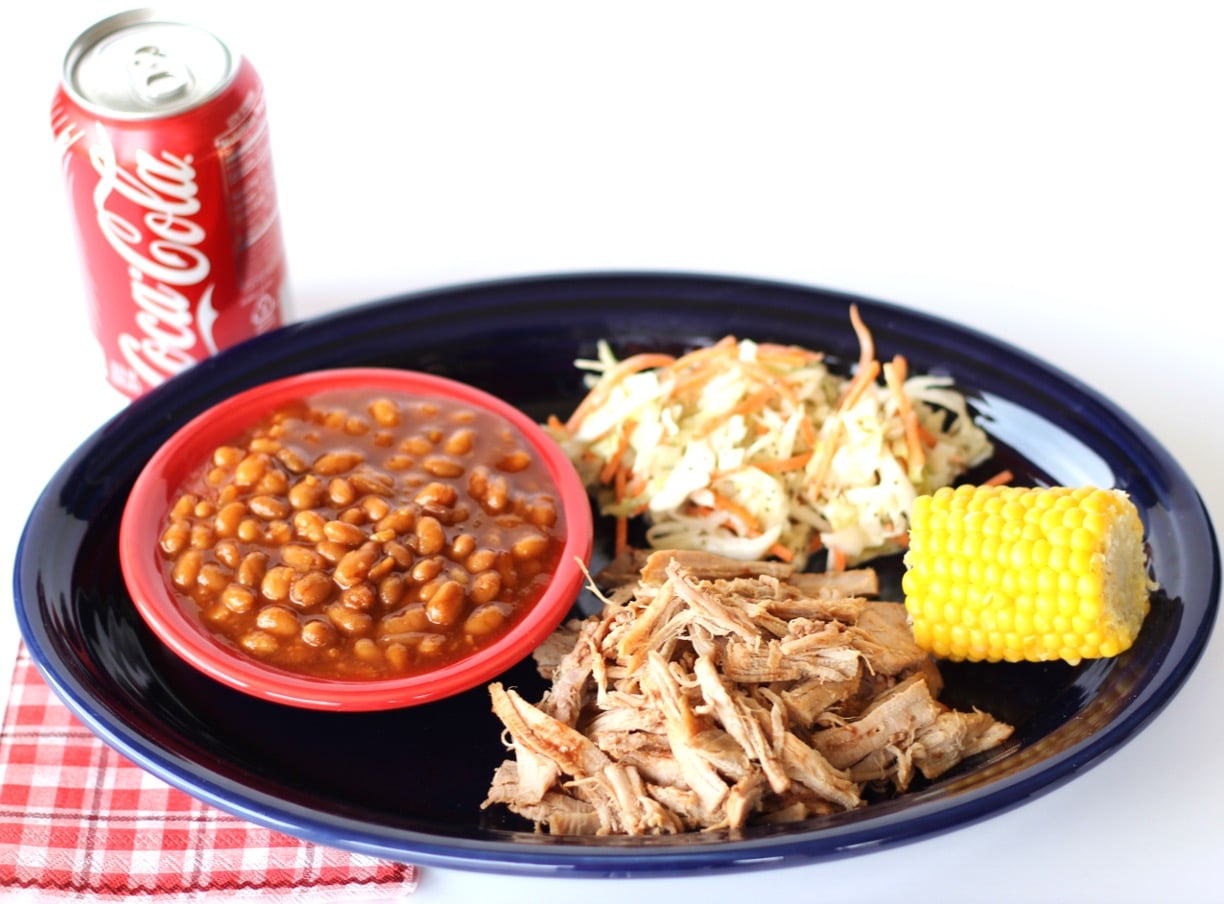 BBQ Pulled pork on plate with barbecue baked beans, coleslaw, and corn on the cob on the side.
