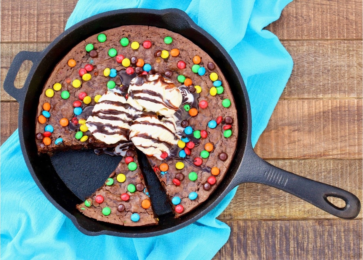 Chocolate brownie in cast iron skillet with scoops of vanilla ice cream in center.