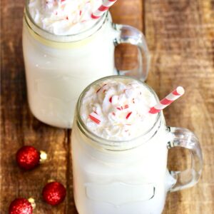Two mason jar mugs filled with white chocolate hot cocoa, with whip cream on top.
