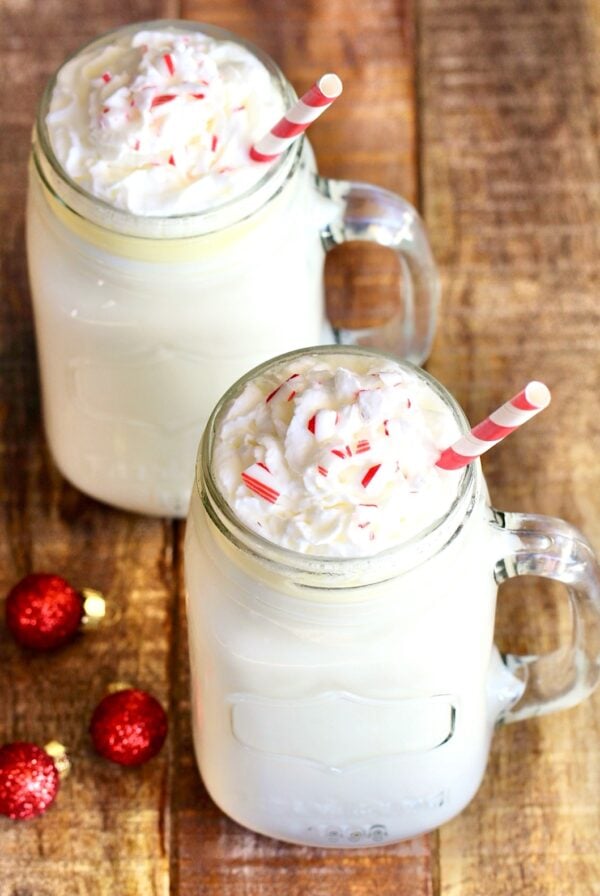 Two mason jar mugs filled with white chocolate hot cocoa, with whip cream on top.