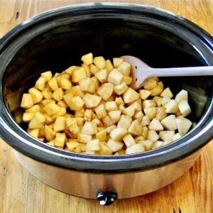 Diced apples in crock pot with wooden spoon.