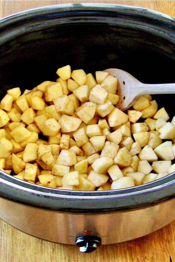Diced apples in crock pot with wooden spoon.