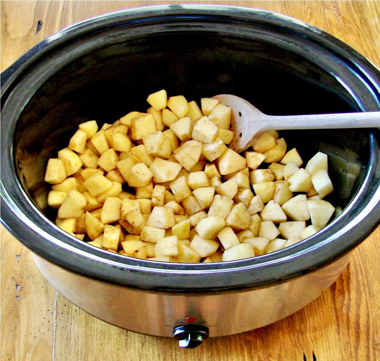 Diced apples in crock pot with wooden spoon.