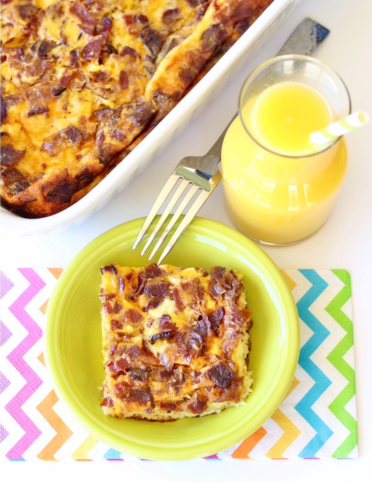 Bacon egg casserole in small dish with orange juice to the side, and 9x13 baking dish in background.