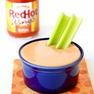 Buffalo ranch sauce in small dish with celery, and bottle of hot wings buffalo sauce in background.
