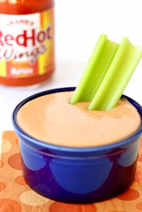 Buffalo ranch sauce in small dish with celery, and bottle of hot wings buffalo sauce in background.
