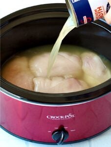 Chicken broth being poured over raw chicken in crock pot.