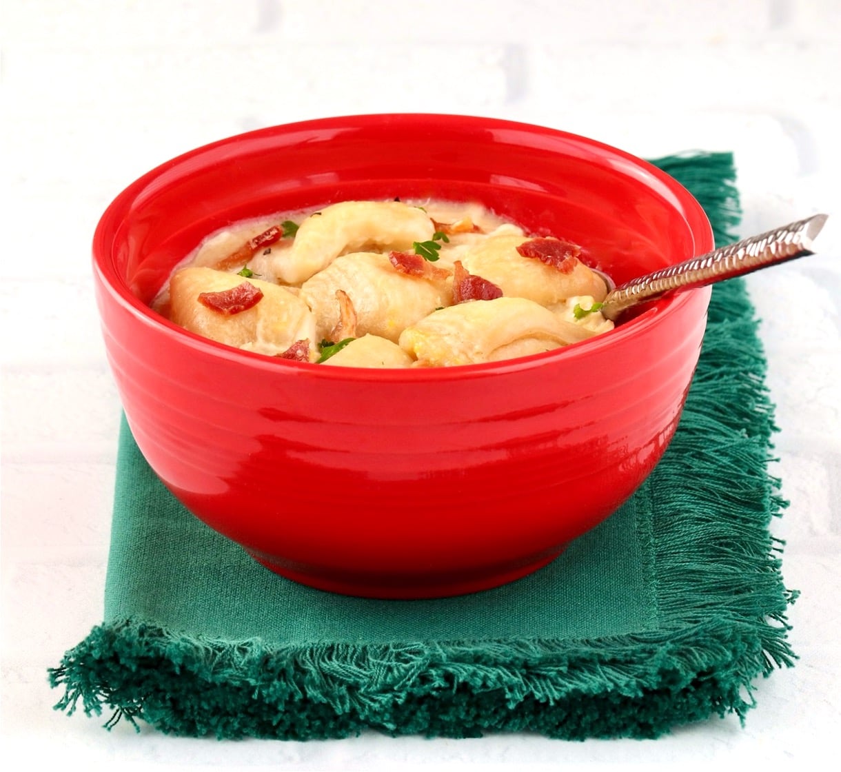 Chicken and dumplings with biscuits in bowl, garnished with bacon and parsley.
