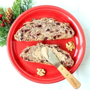Two slices of cranberry walnut bread on plate with butter being spread on one slice.