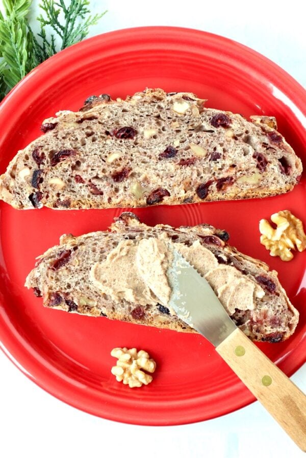 Two slices of cranberry walnut bread on plate with butter being spread on one slice.