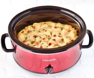 Chicken and dumplings with biscuits in crockpot, garnished with bacon and parsley.