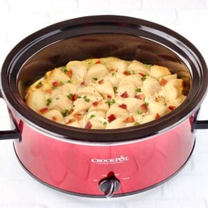 Chicken and dumplings with biscuits in crockpot, garnished with bacon and parsley.