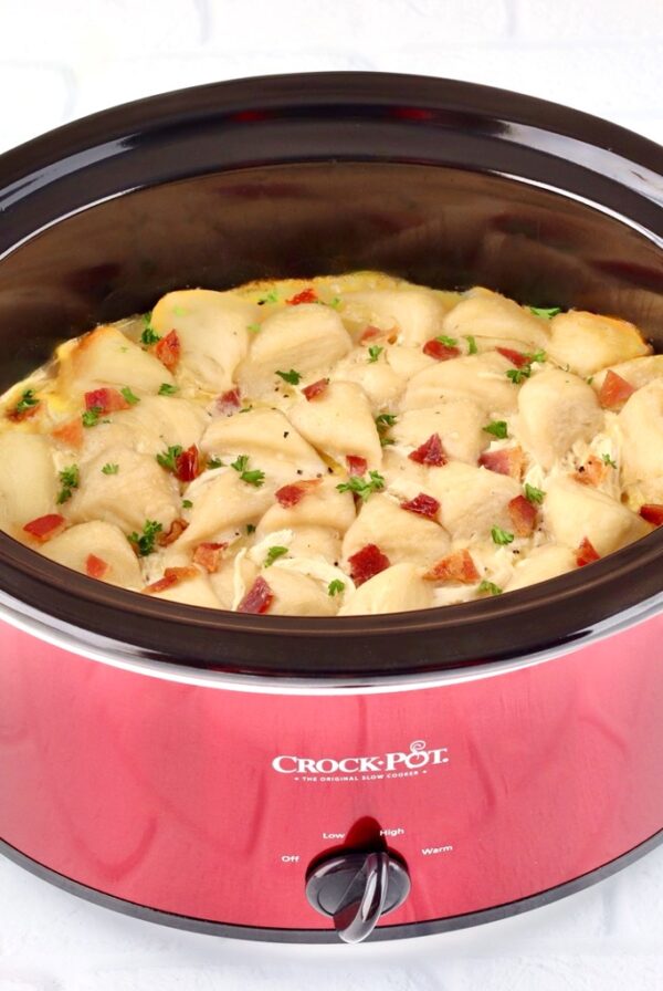 Chicken and dumplings with biscuits in crockpot, garnished with bacon and parsley.