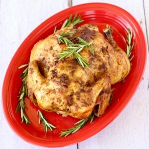 Whole chicken on red platter with rosemary.