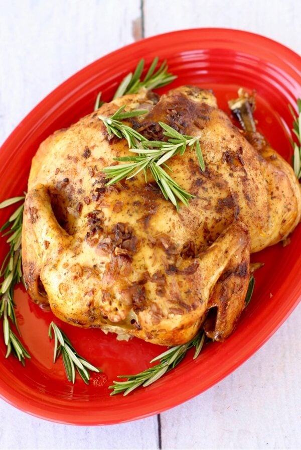 Whole chicken on red platter with rosemary.