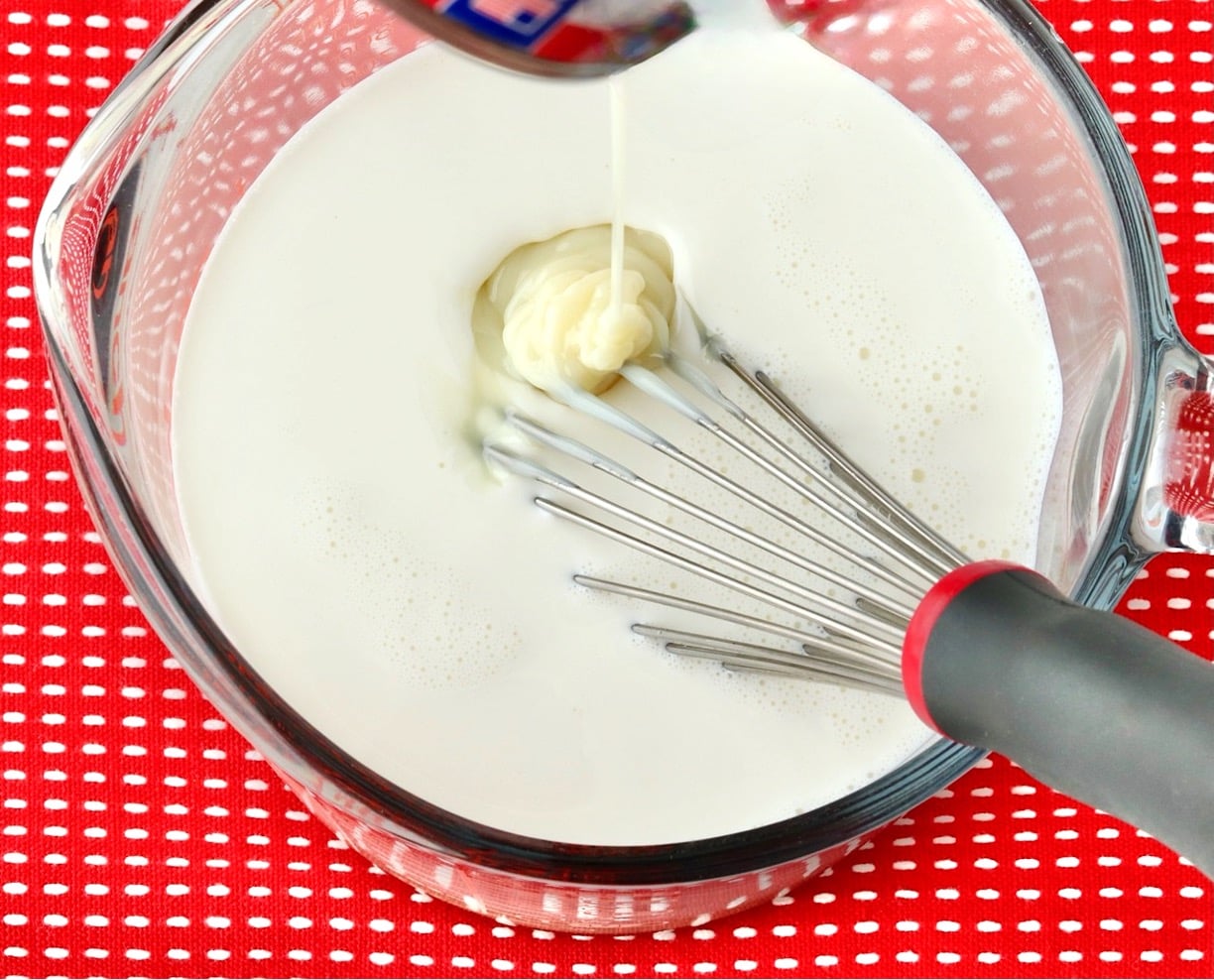 Sweetened condensed milk pouring into homemade coffee creamer in large measuring cup with whisk.