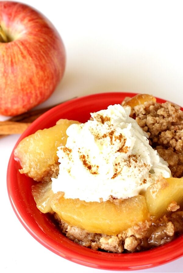 Apple spice dump cake in small bowl with whip cream on top.