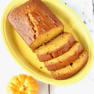 Homemade moist loaf of pumpkin bread on plate with three slices and rest of loaf.