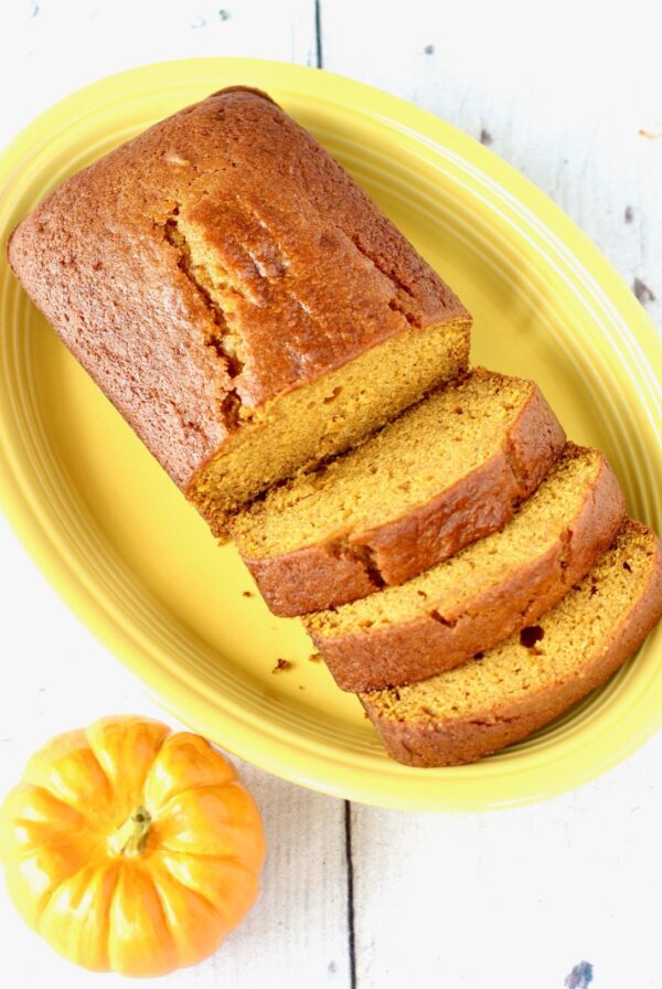 Homemade moist loaf of pumpkin bread on plate with three slices and rest of loaf.