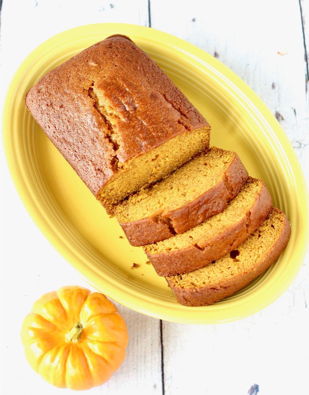 Homemade moist loaf of pumpkin bread on plate with three slices and rest of loaf.