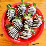 Chocolate covered strawberries with white chocolate drizzle on red plate.