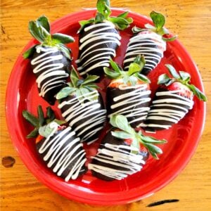 Chocolate covered strawberries with white chocolate drizzle on red plate.