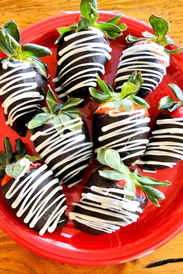 Chocolate covered strawberries with white chocolate drizzle on red plate.