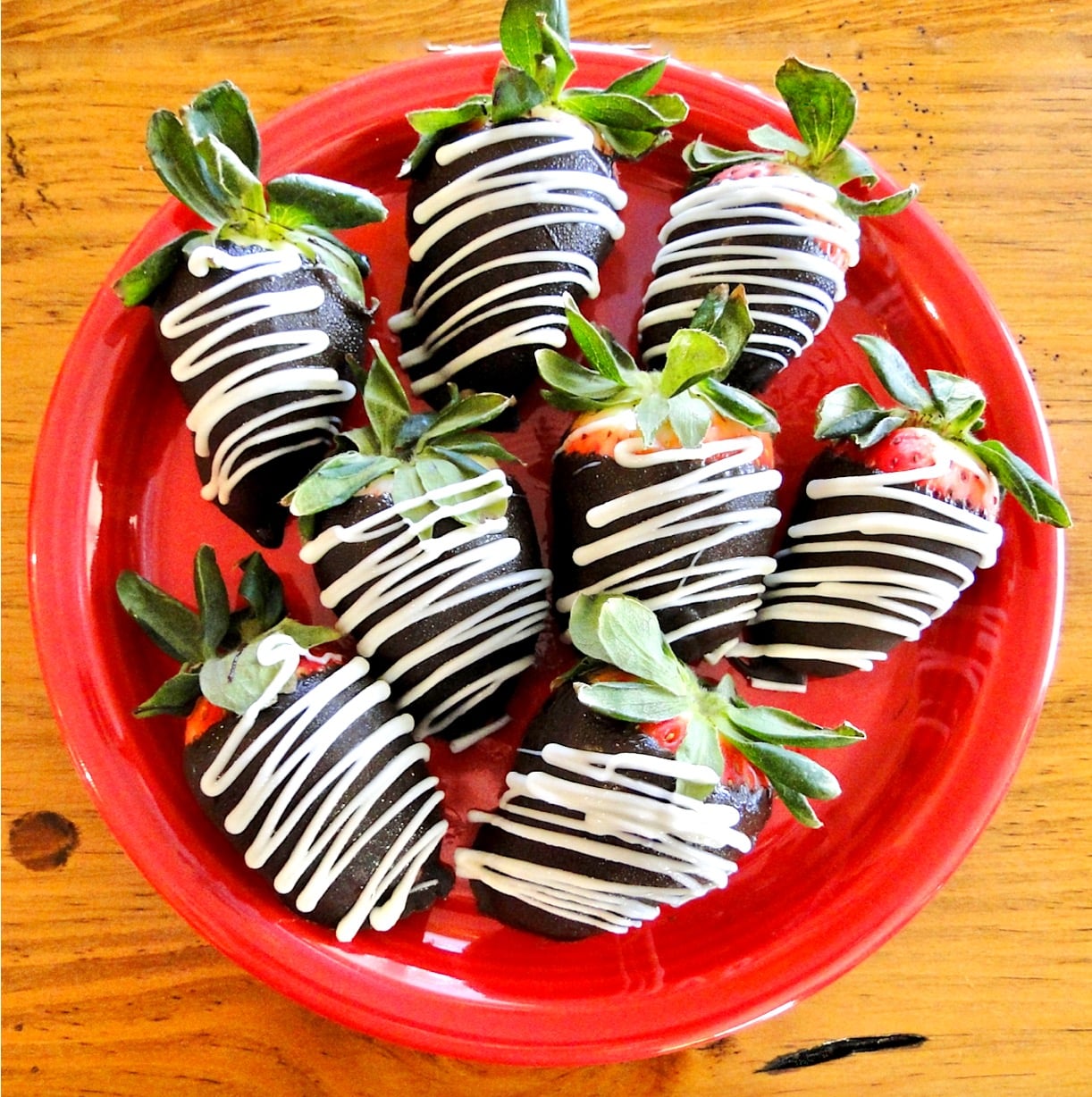 Chocolate covered strawberries with white chocolate drizzle on red plate.