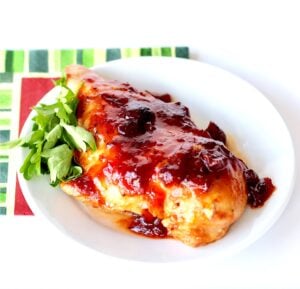 Piece of chicken with cranberry orange sauce on top on plate.