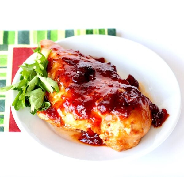 Piece of chicken with cranberry orange sauce on top on plate.