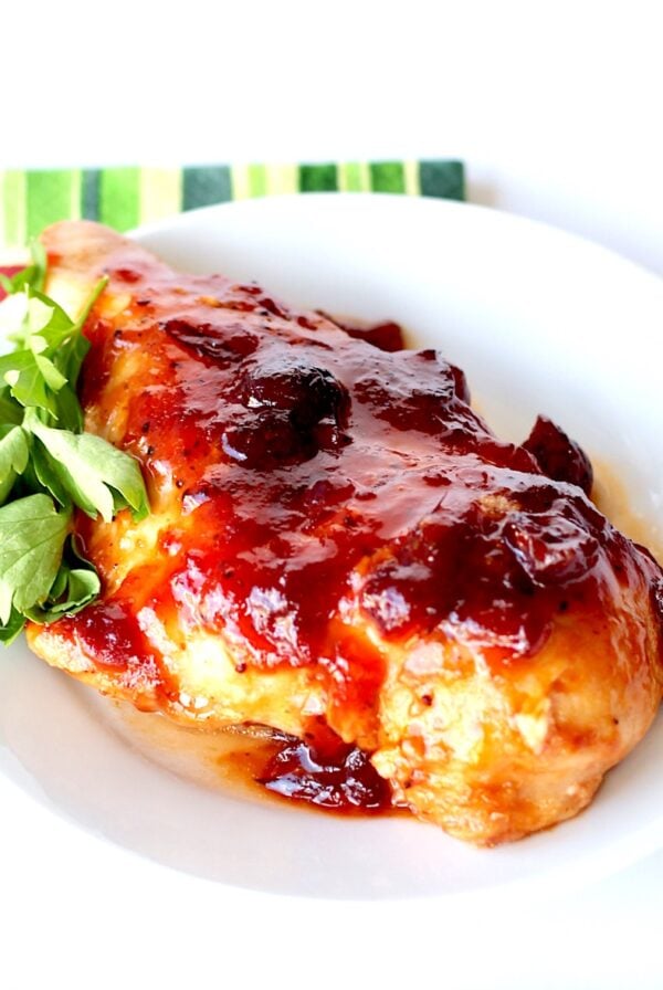 Piece of chicken with cranberry orange sauce on top on plate.