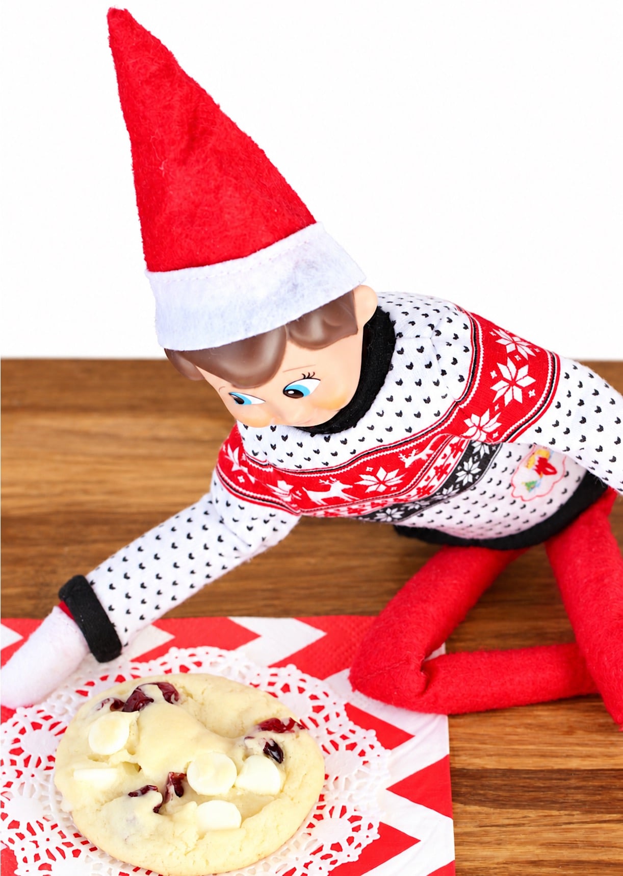 Elf on the shelf looking at cranberry white chocolate chip cookie on napkin.