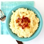 Crockpot cheesy potatoes in small dish, topped with crispy bacon.