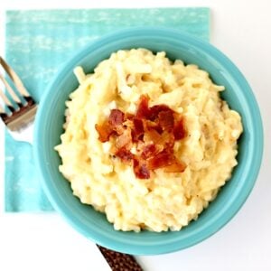 Crockpot cheesy potatoes in small dish, topped with crispy bacon.