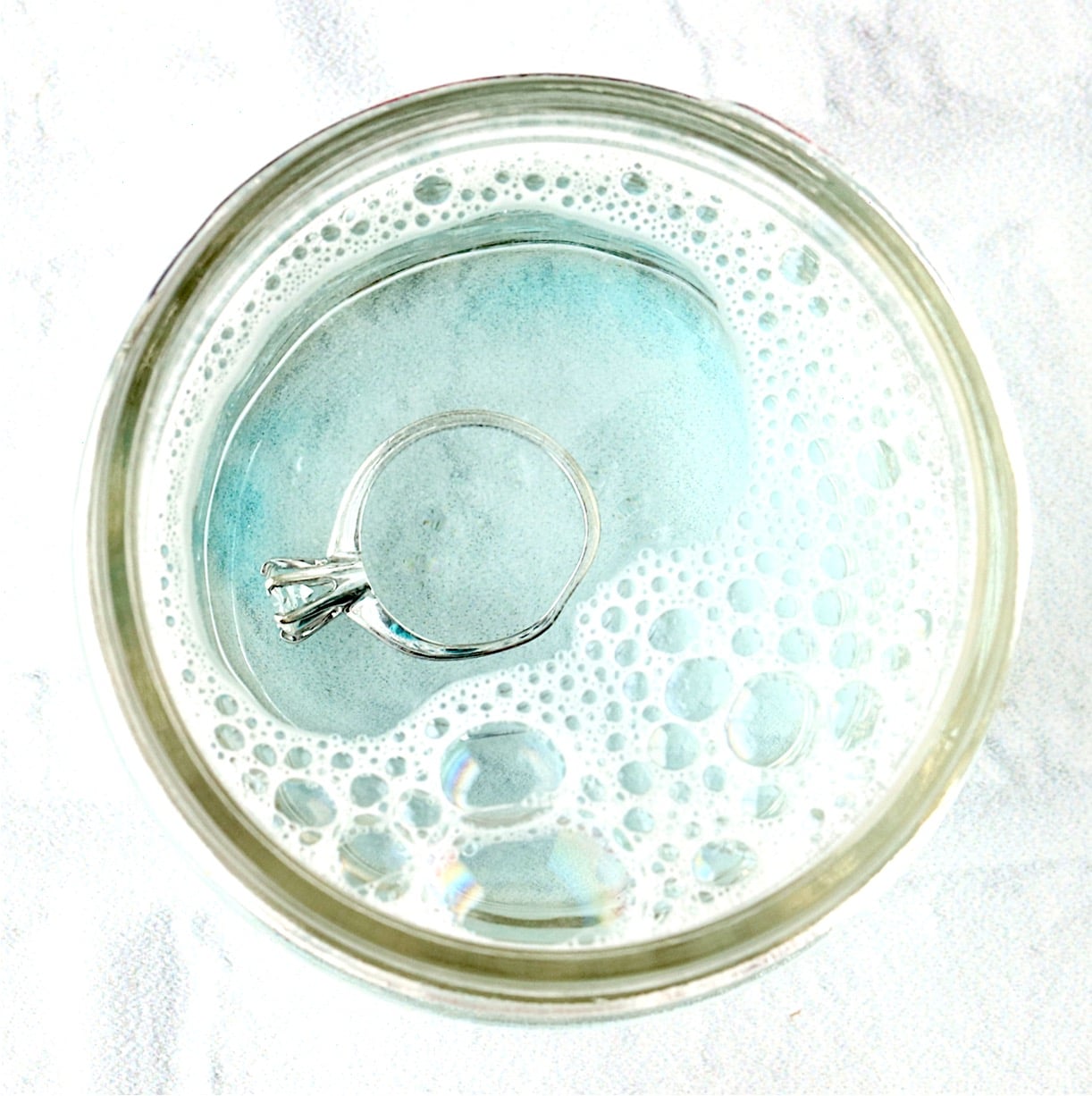 Diamond ring jewelry being cleaned at home with dawn dish soap solution.