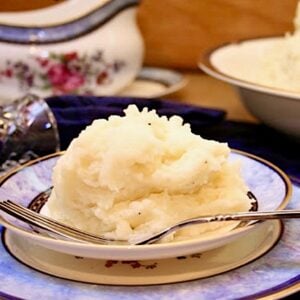 Fluffy mashed potatoes on plate with fork, and bowl of mashed potatoes in background.
