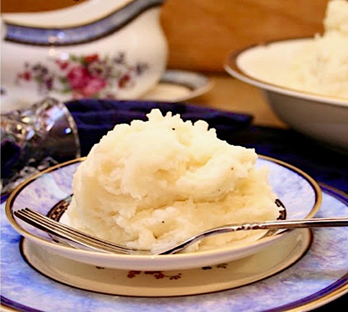 Fluffy mashed potatoes on plate with fork, and bowl of mashed potatoes in background.