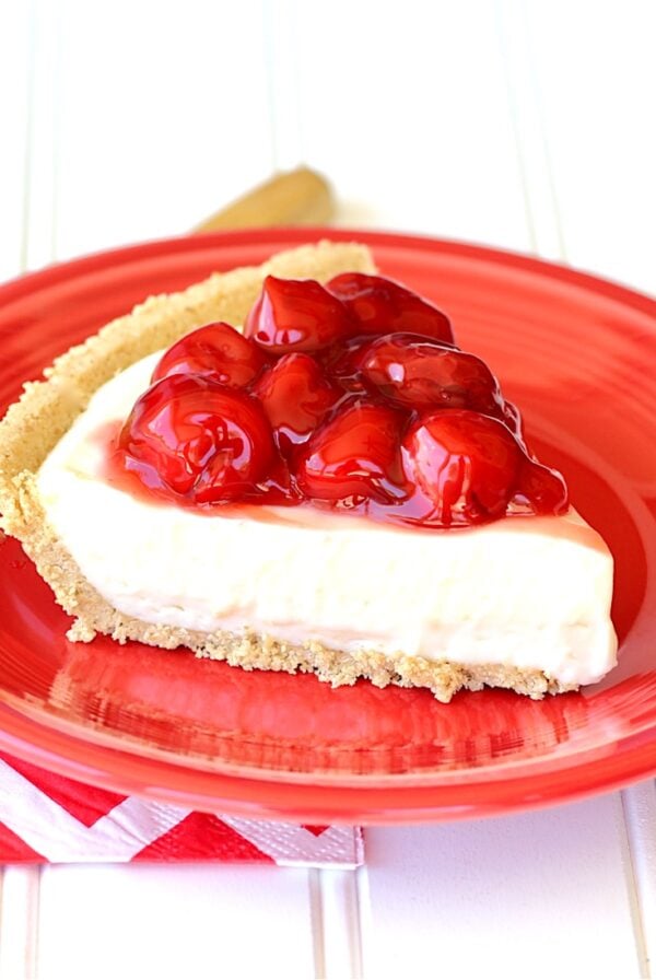 Slice of no bake cherry cheesecake on red plate with napkin to the side.