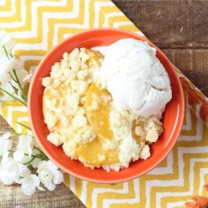 Peach cobbler made with cake mix in small bowl with scoop of vanilla ice cream.