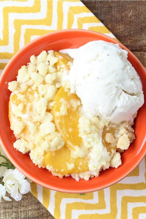 Peach cobbler made with cake mix in small bowl with scoop of vanilla ice cream.