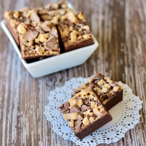 Two squares of chocolate Toffee Fudge, with more pieces in dish in background.