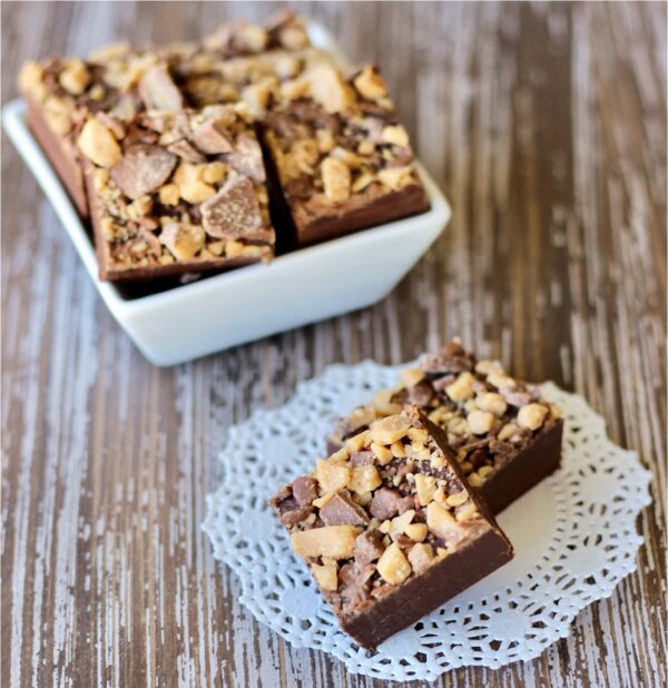 Two squares of chocolate Toffee Fudge, with more pieces in dish in background.
